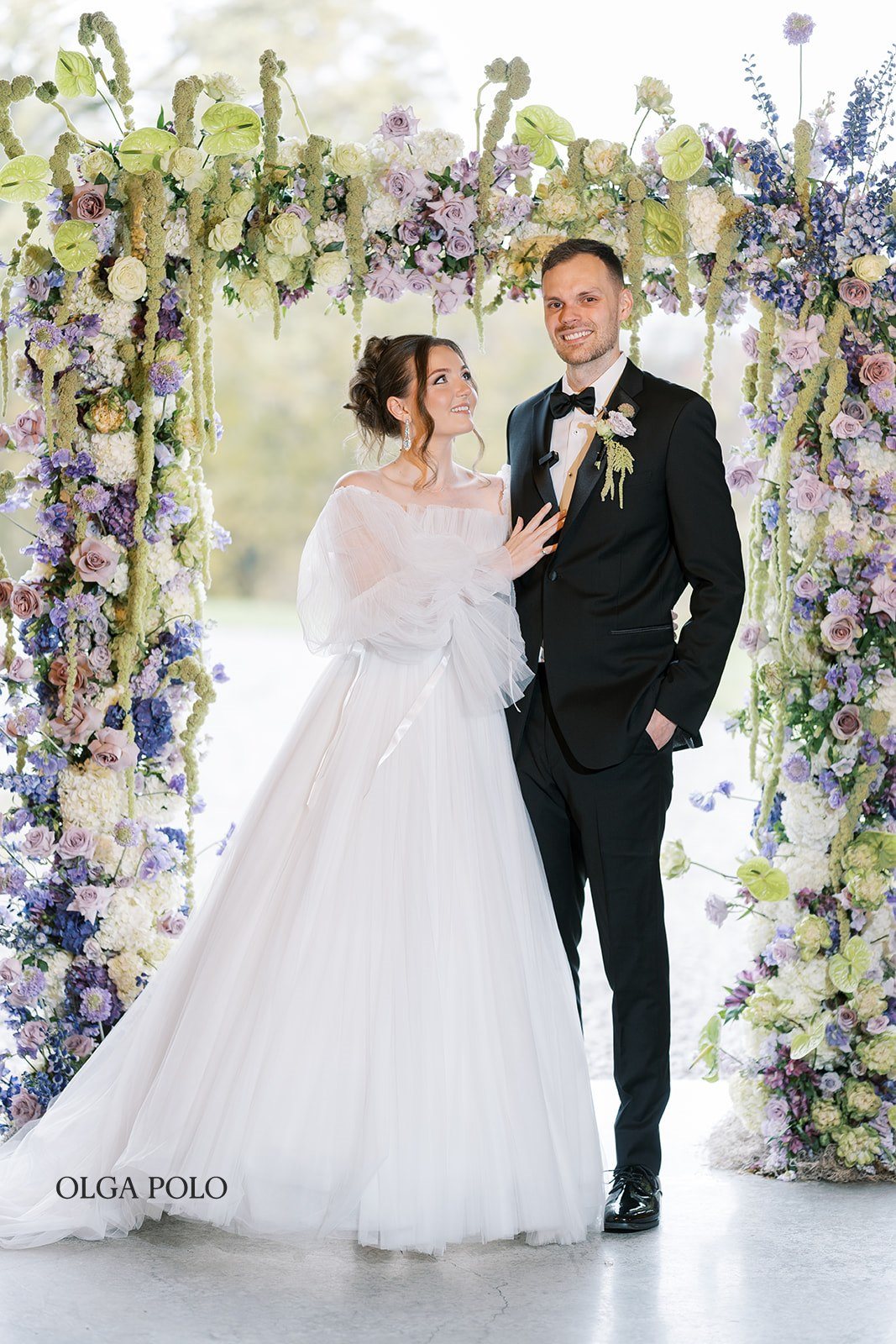 Maia and Troy posing together beneath the ceremony florals