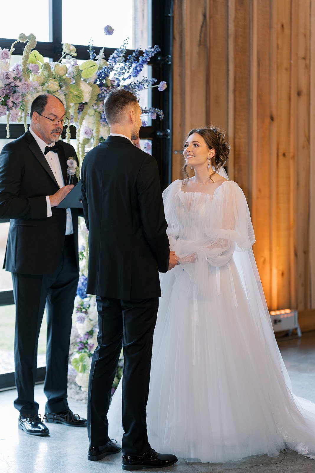 Maia and Troy exchanging vows beneath the floral ceremony installation