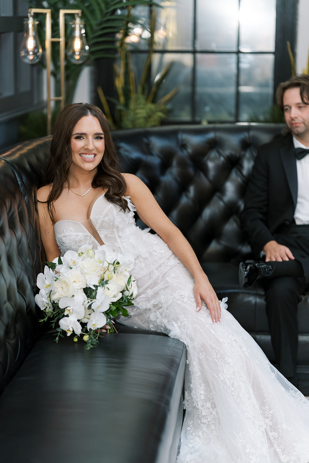 Ronnie and Patrick seated together on a dark leather sofa for a wedding portrait