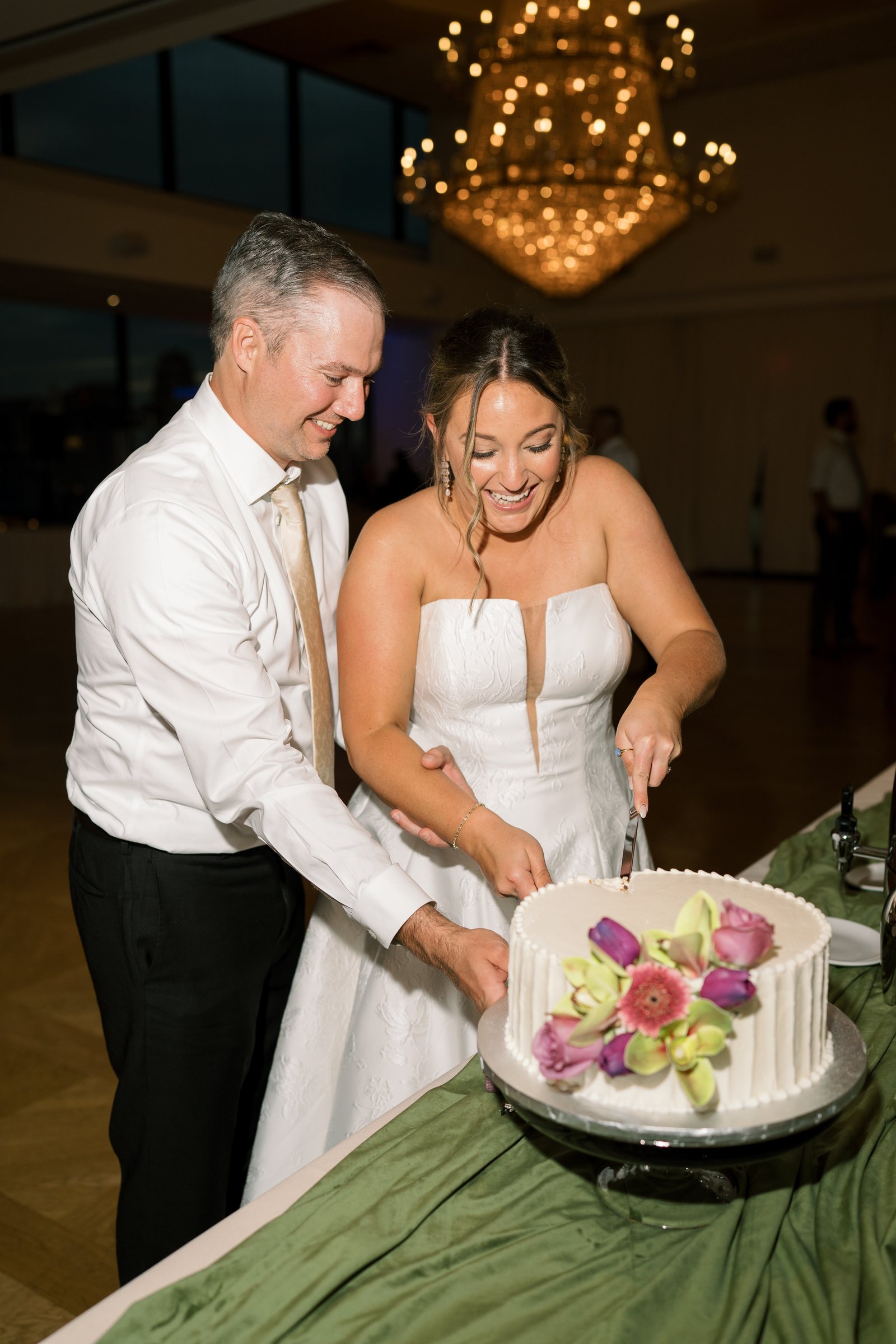 Kent and Nicolette cutting their white floral wedding cake
