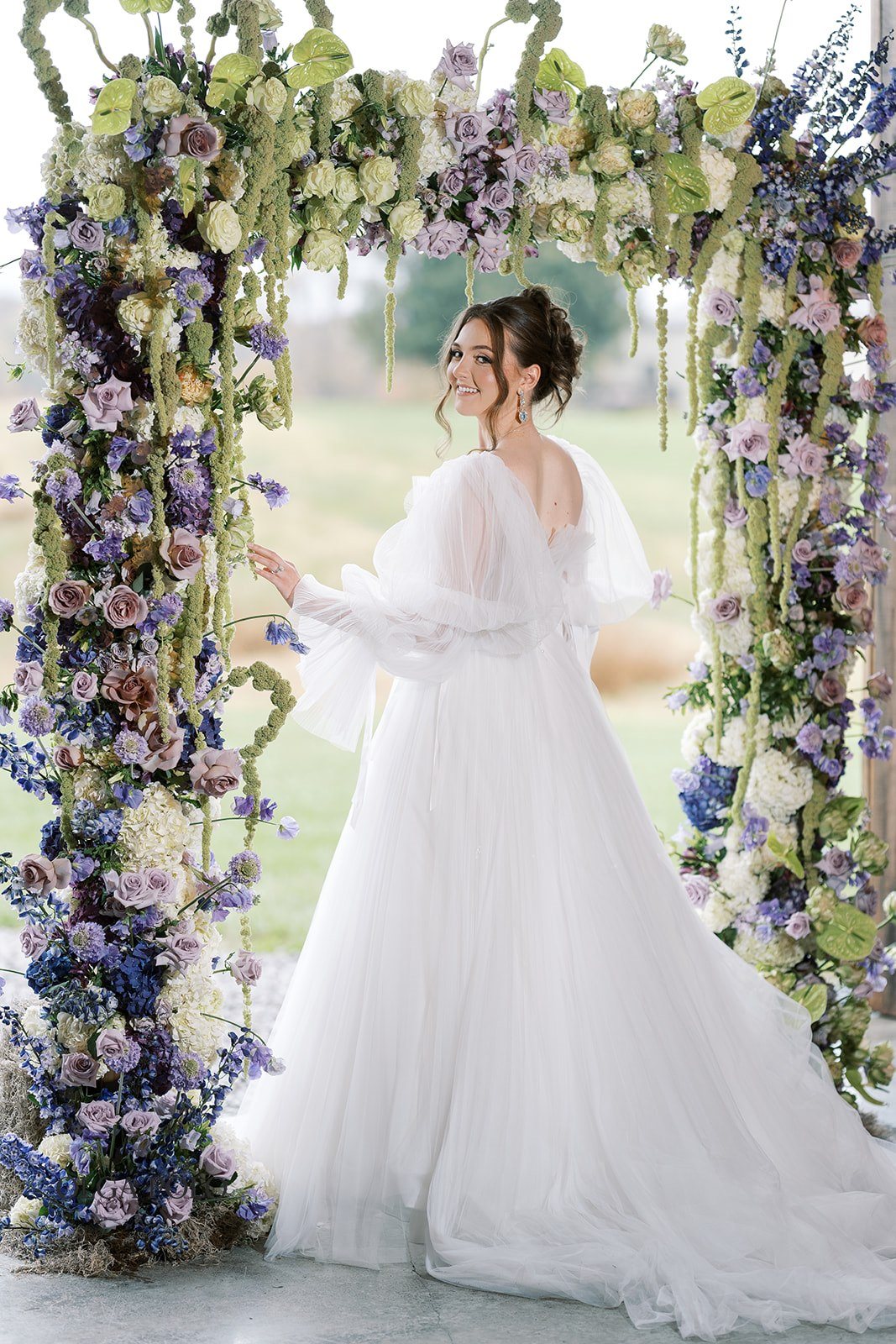 Maia beneath the purple and green floral ceremony installation