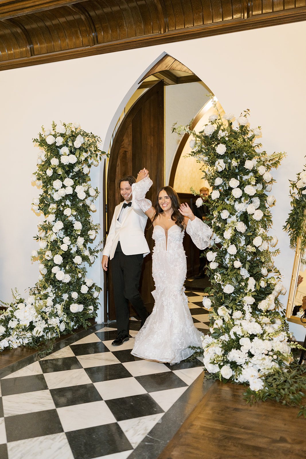 Ronnie and Patrick beneath a white floral arch on The Palomar Cincinnati's checkerboard floor