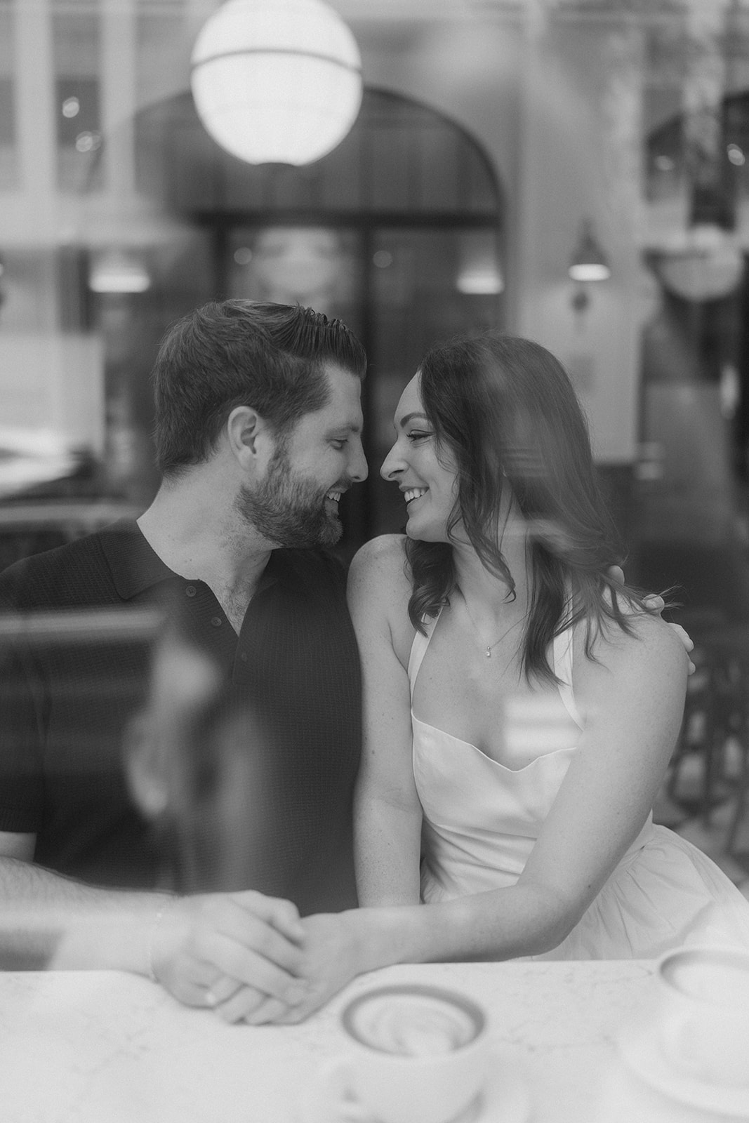 Black-and-white portrait of Frank and Noelle seated together through a café window