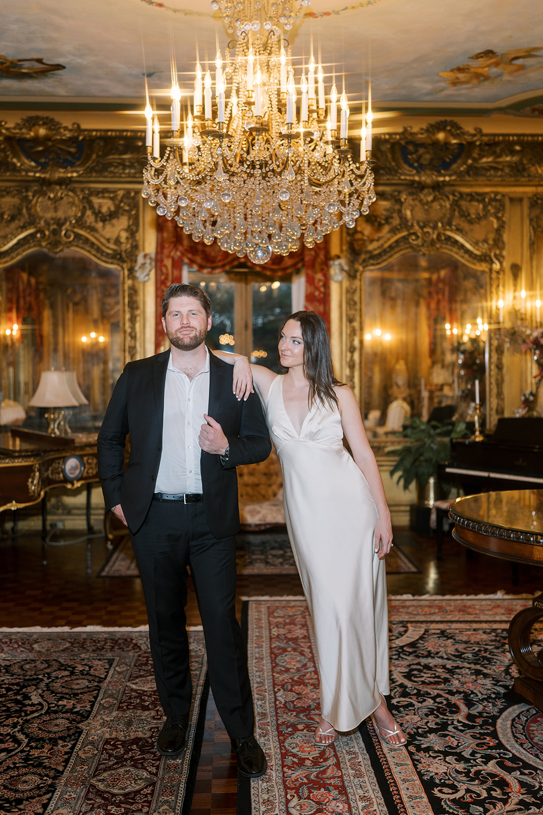 Frank and Noelle standing beneath a chandelier in Laurel Court's gilded interior