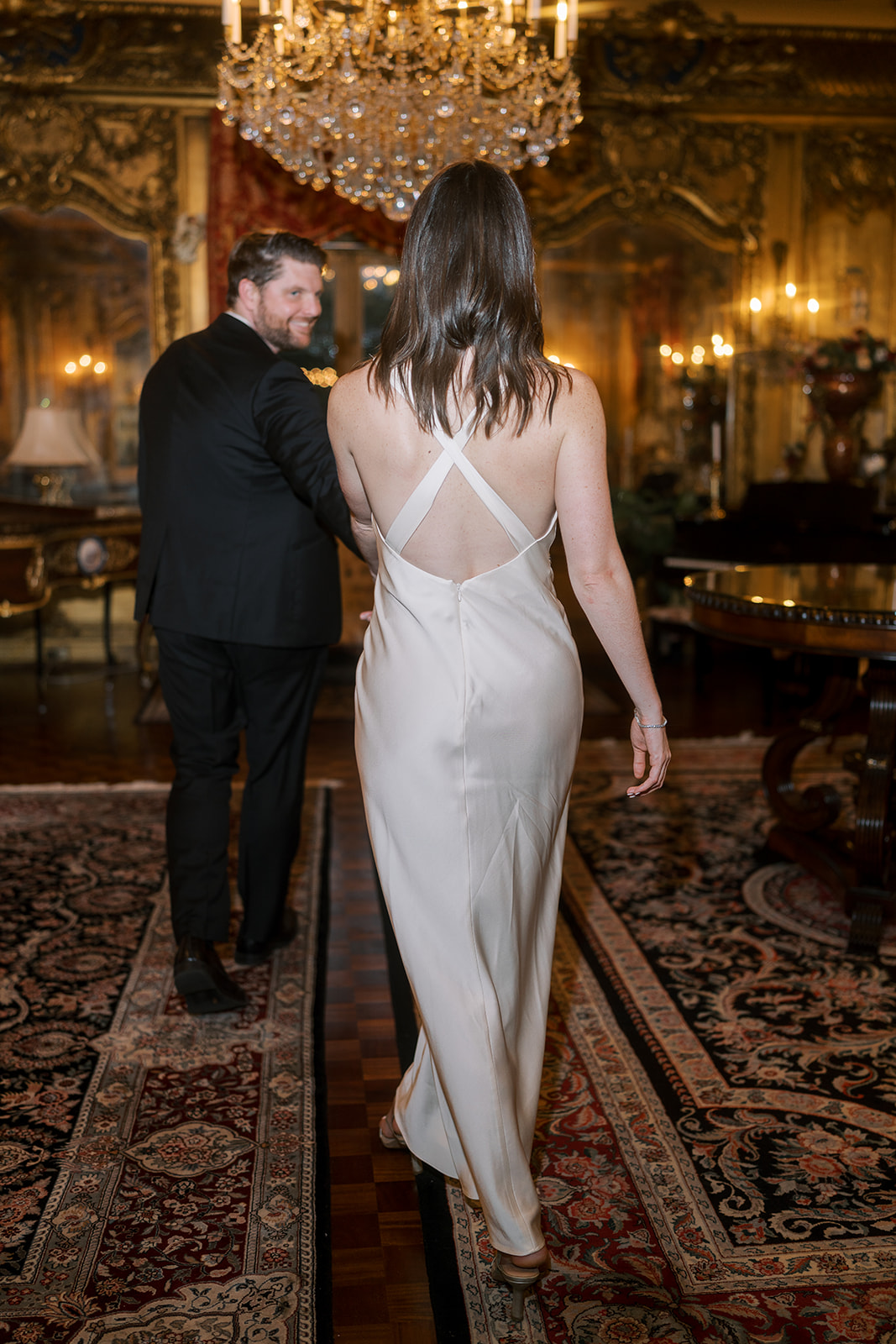 Frank and Noelle walking into a gilded chandelier-lit room at Laurel Court