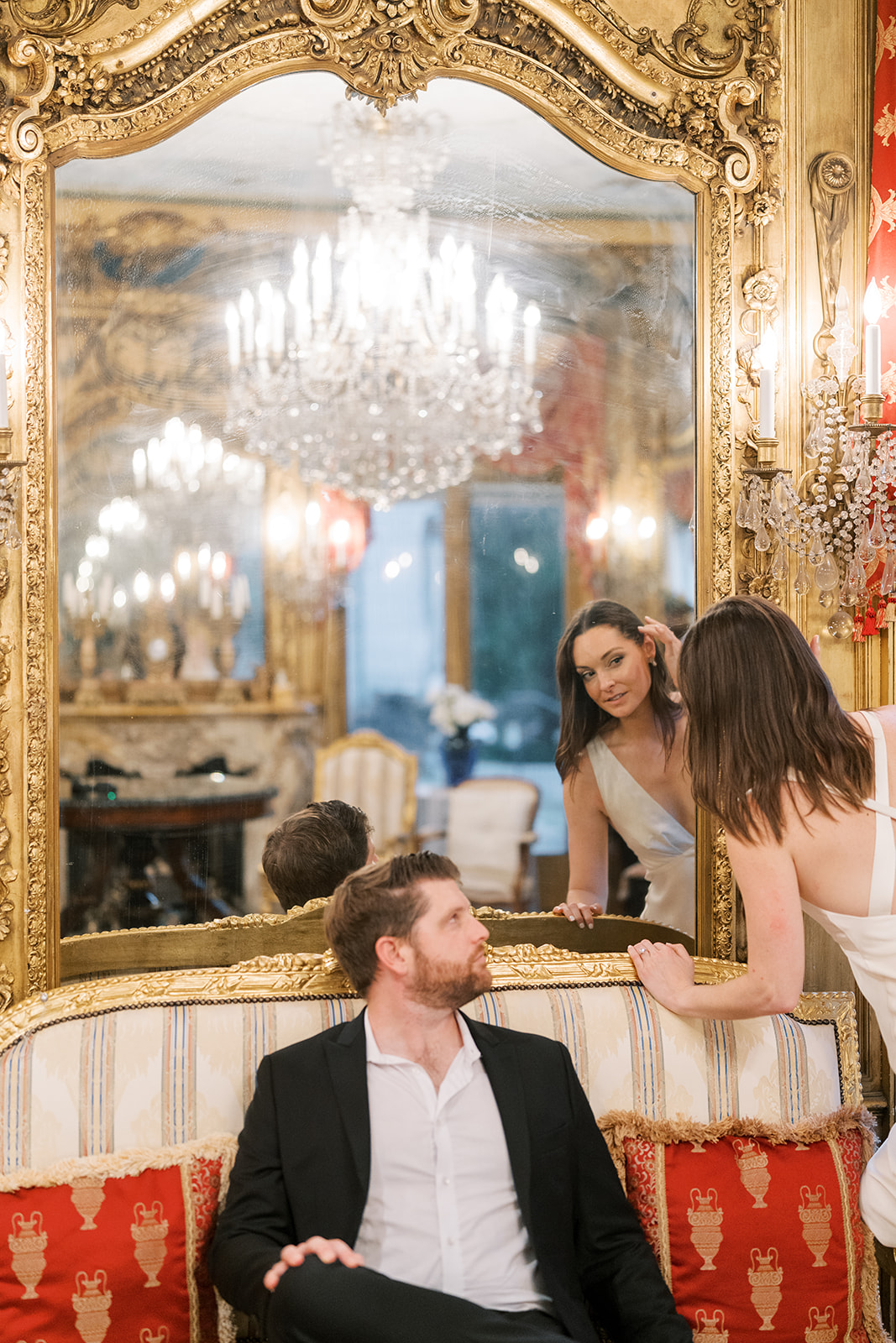 Frank and Noelle framed by a large gilded mirror and red settee at Laurel Court