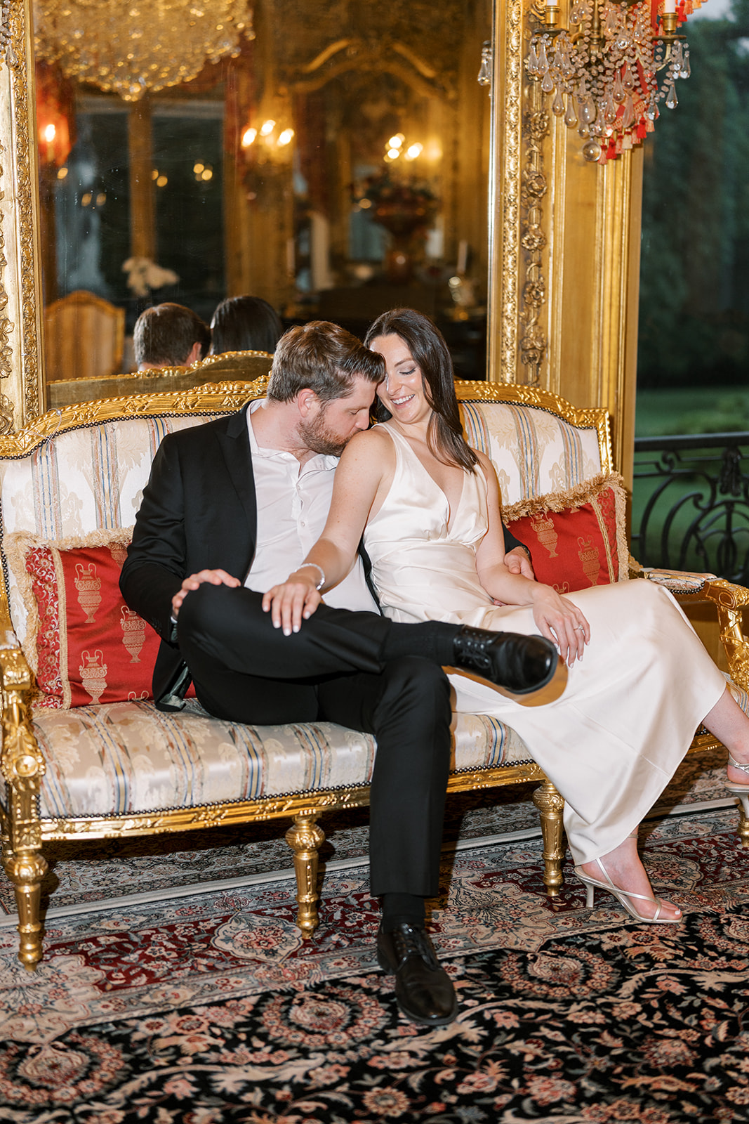 Frank and Noelle seated together on a red settee inside Laurel Court