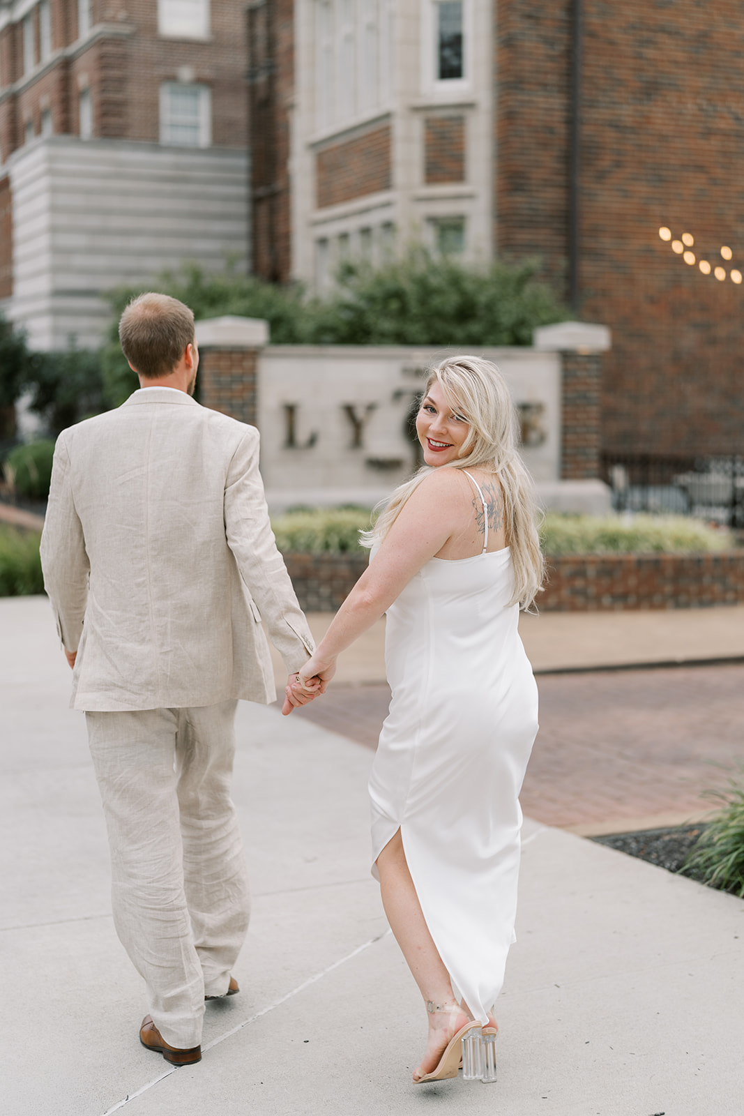 Josh and Autumn walking hand in hand near The Lytle Park Hotel sign
