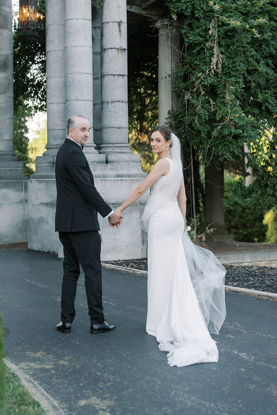 Michael and Julia holding hands near the classical columns and gardens at Laurel Court