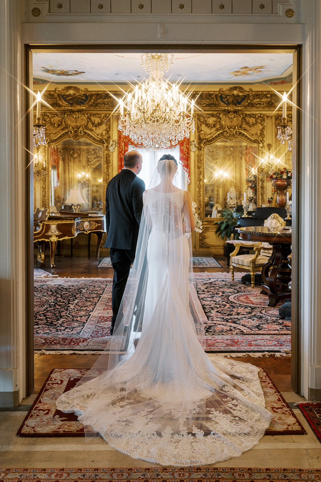 Michael and Julia posing beneath a crystal chandelier in the gilded room at Laurel Court
