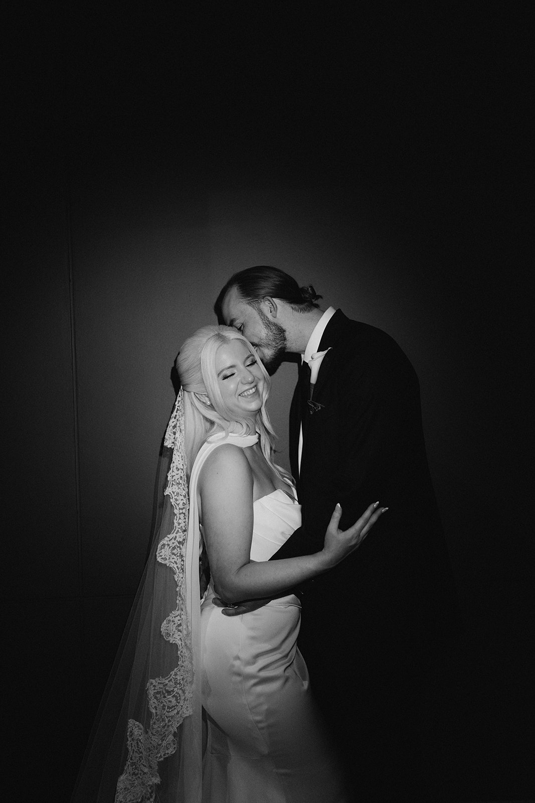 Black-and-white close portrait of Niamh and Titus kissing in front of the red gallery wall