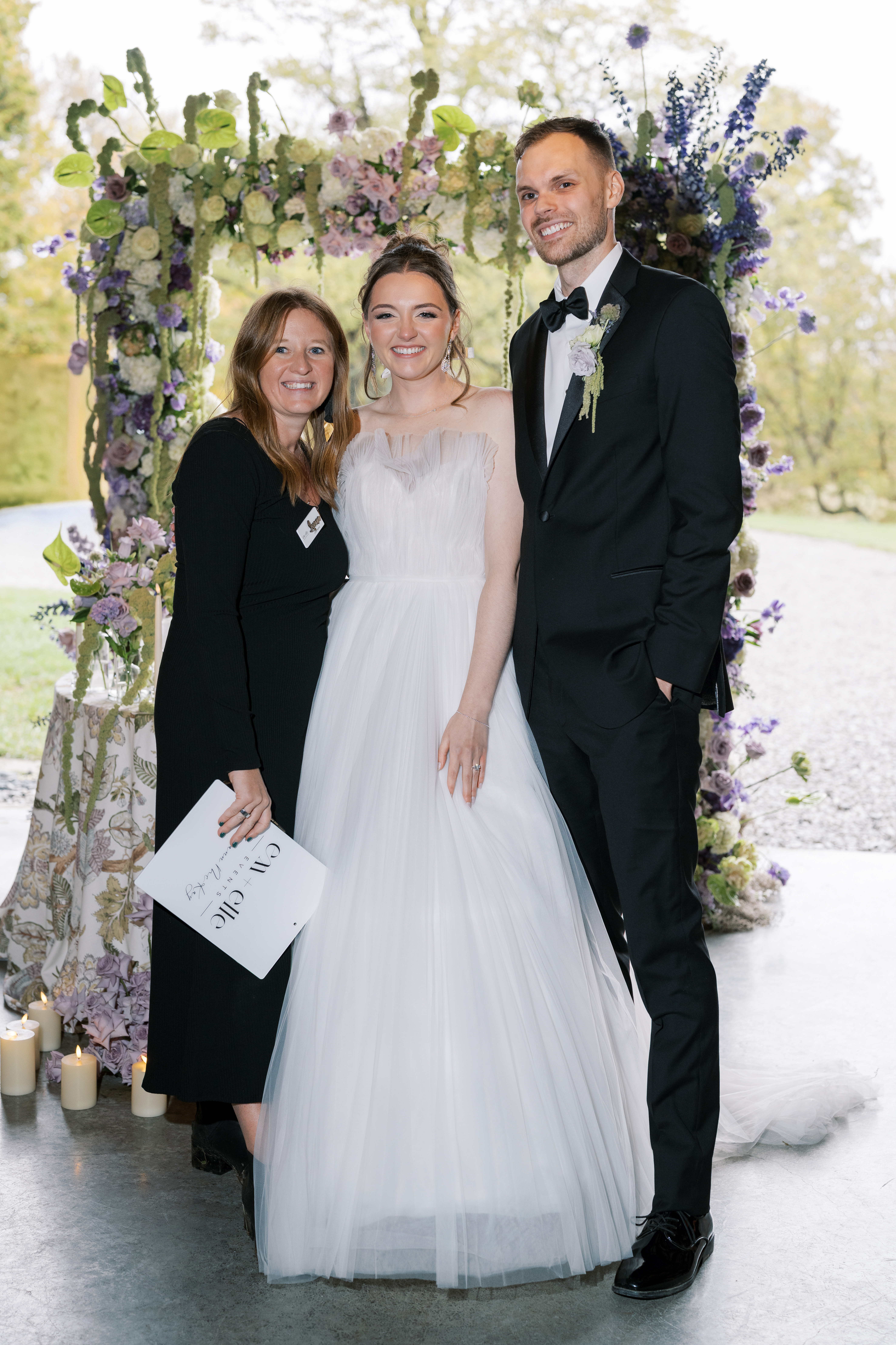 Leeann McKay of Em + Elle Events with the bride and groom beneath a floral ceremony arch
