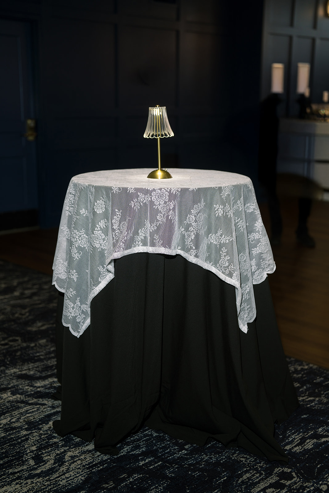 Black cocktail table with lace overlay and a small lamp at the reception