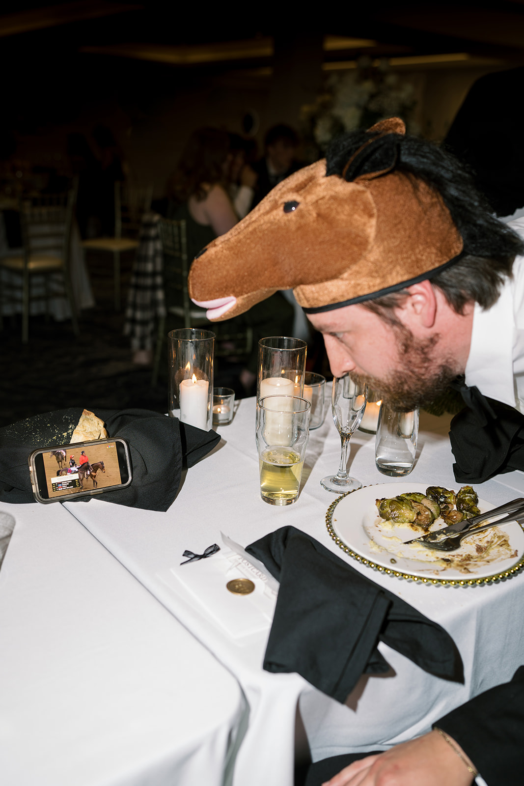 Wedding guest wearing a playful horse-head hat during dinner