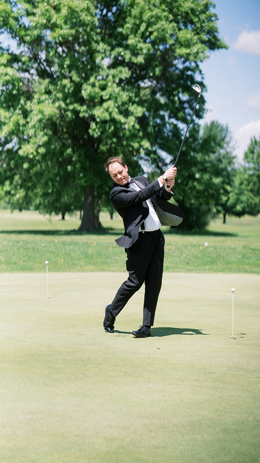 Ben swinging a golf club on a putting green before the wedding