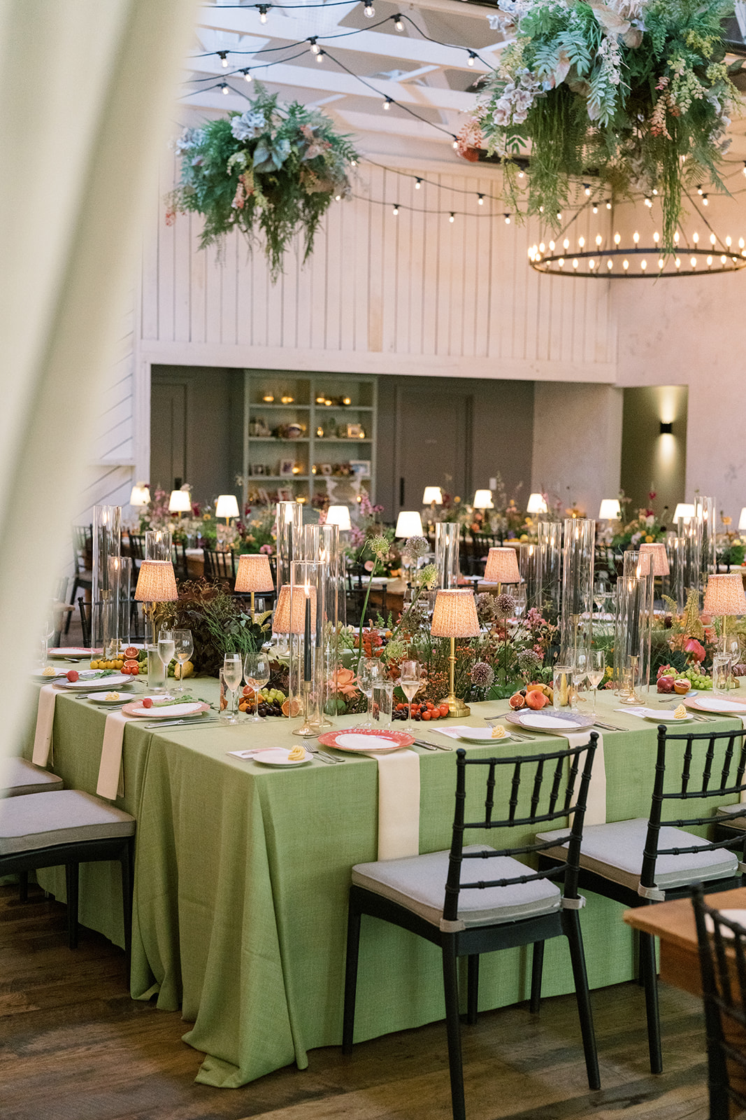 Reception room with green linens, garden florals and chandeliers at Terrain Gardens at DelVal