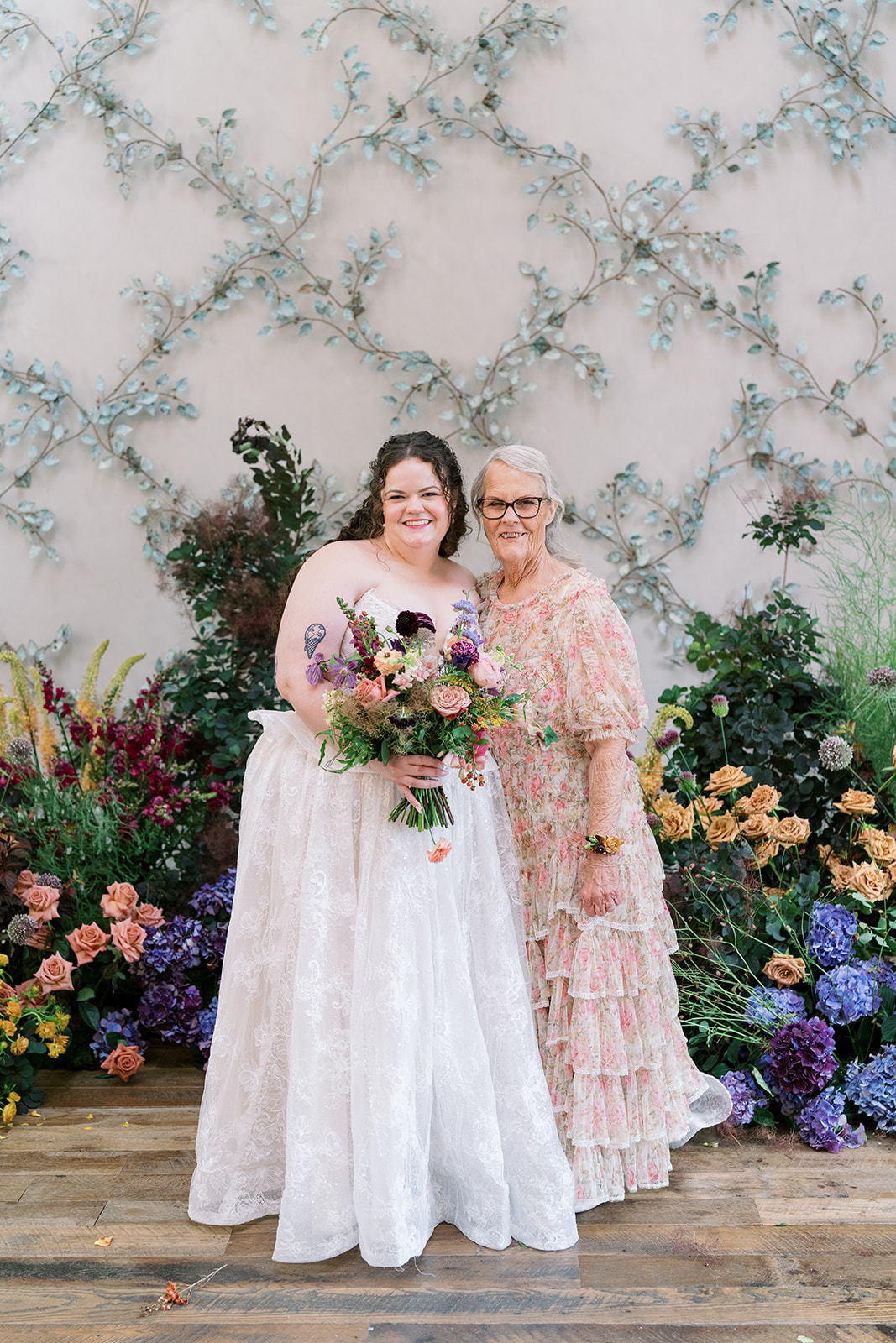 Bride posing with a family member or guest at the floral ceremony backdrop