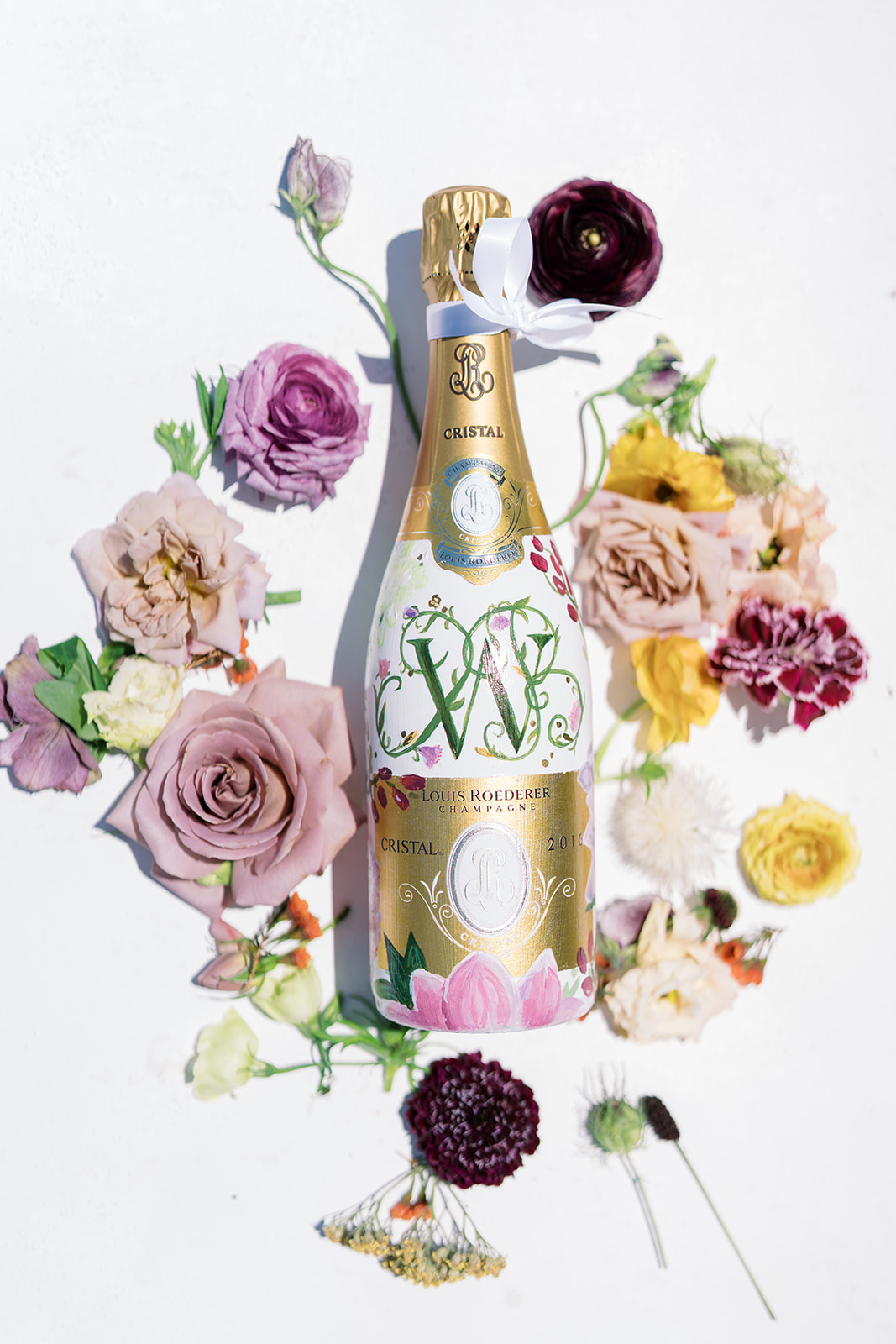 Monogrammed bottle and flowers in a styled wedding flat lay