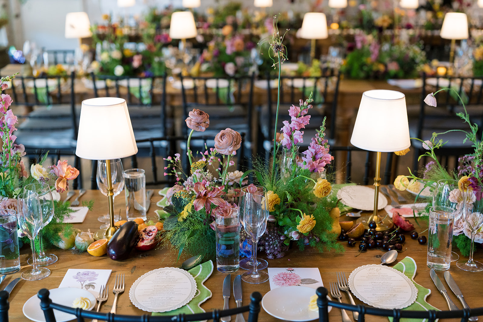 Reception table set with lamps, flowers, glassware and seasonal fruit