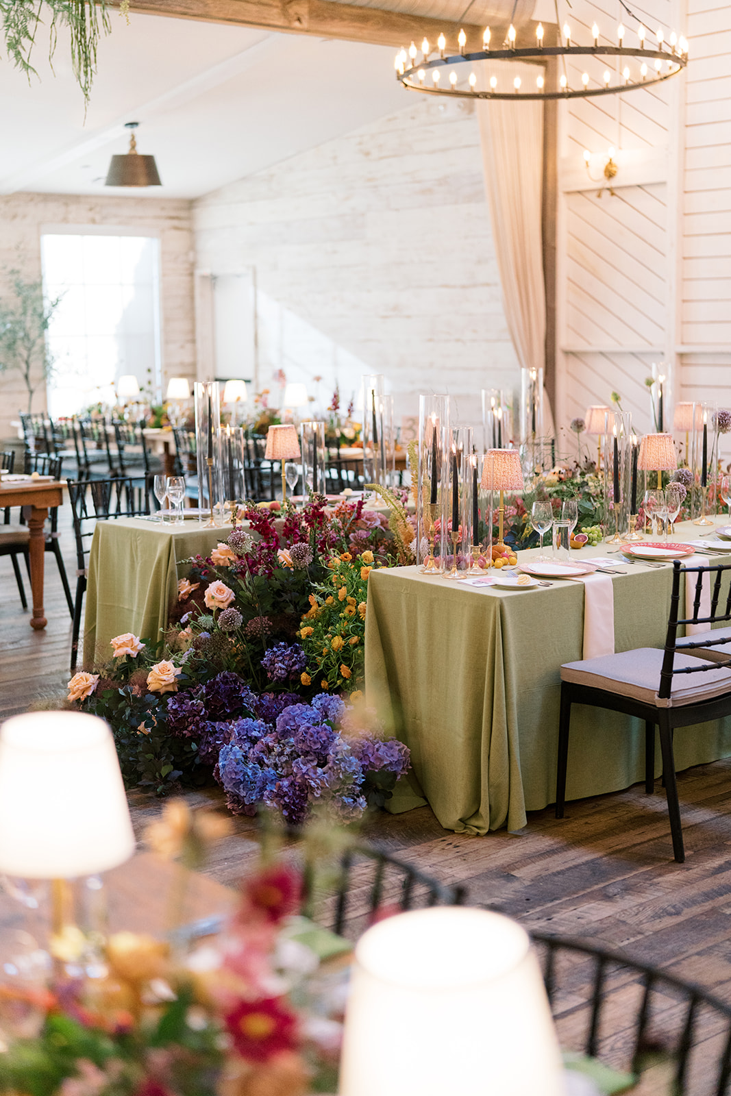 Wide view of the reception room with chandeliers, green linens and colorful flowers