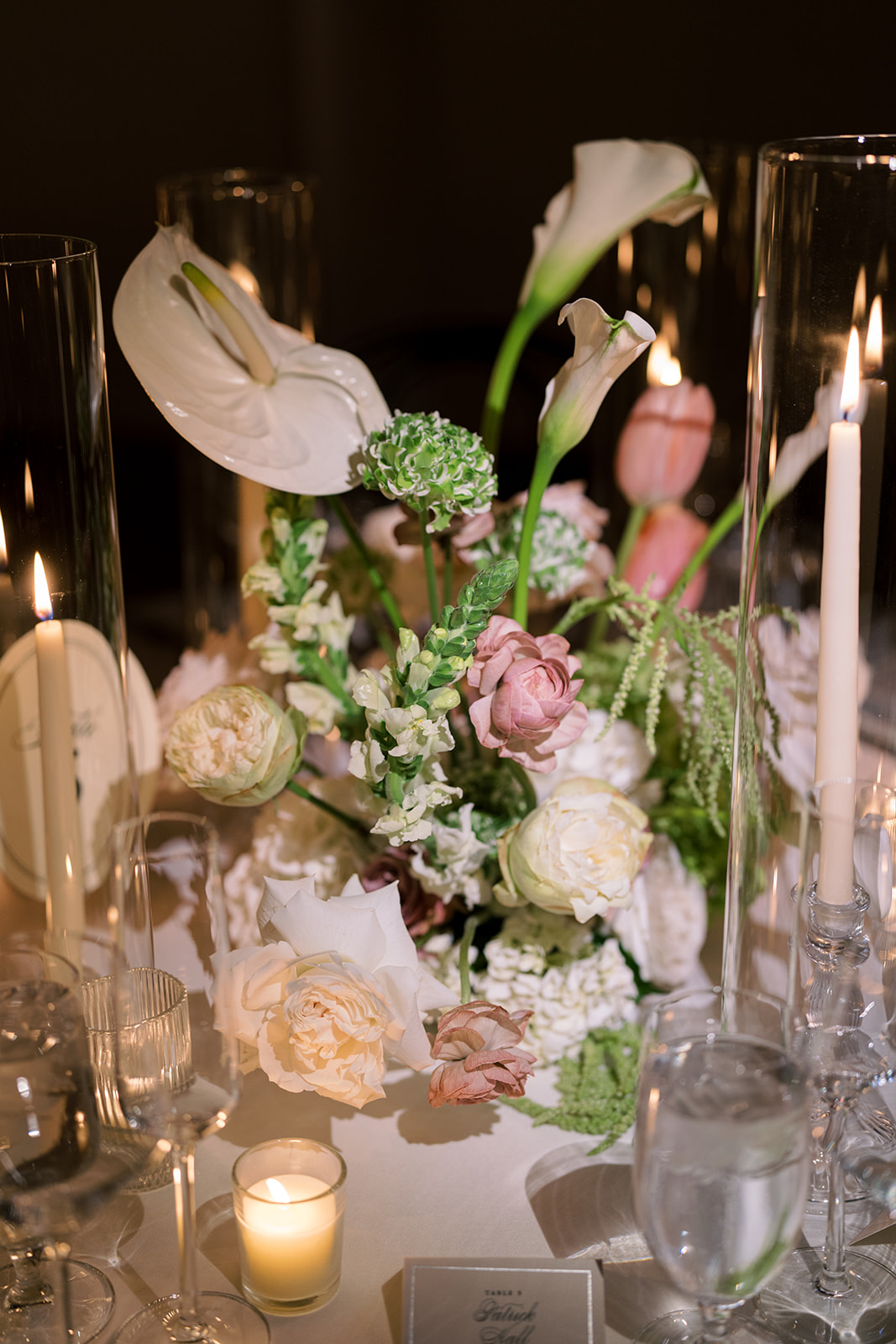 Pink orchid and floral centerpiece glowing among reception candles
