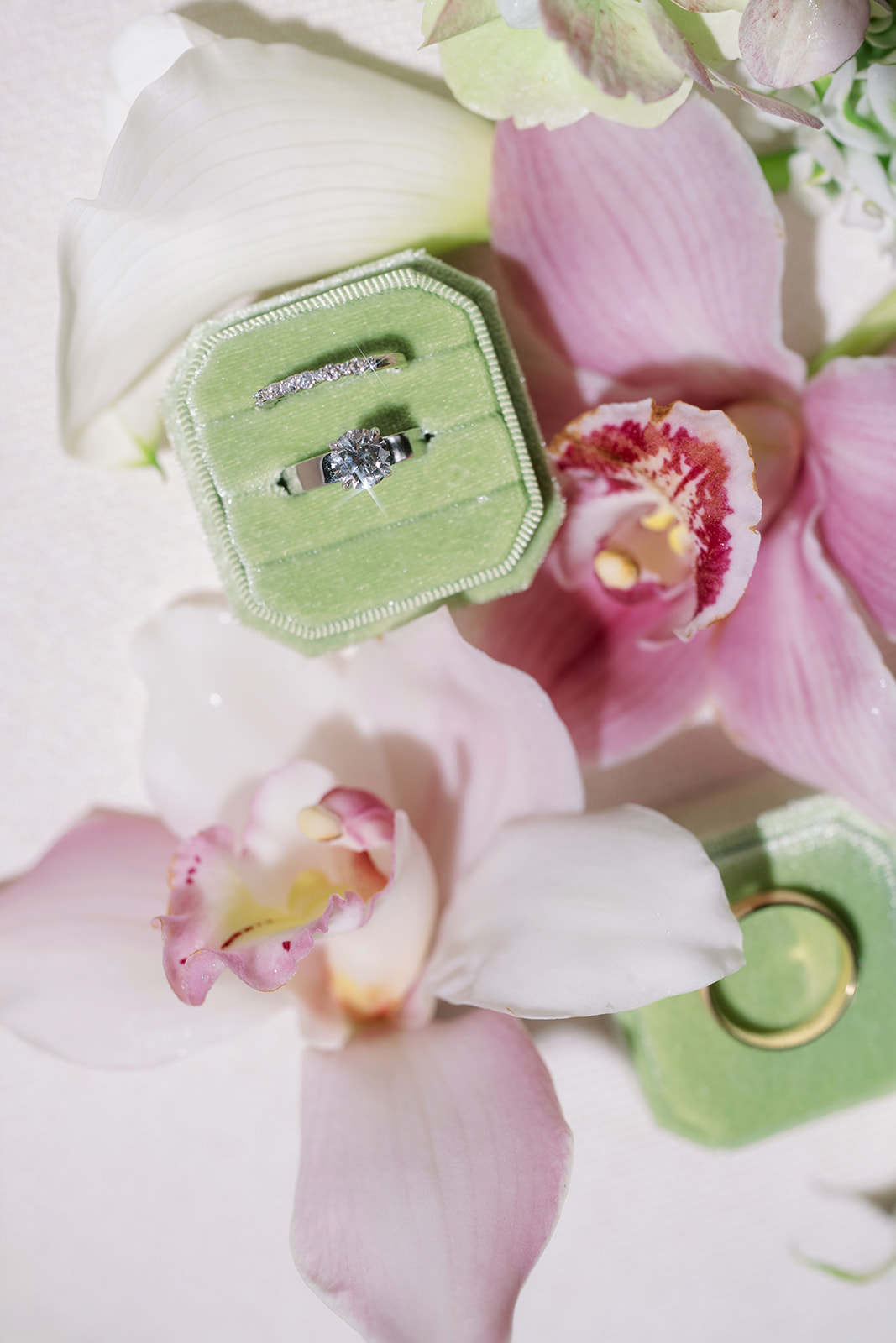 Green perfume bottle arranged among pink orchids and bridal details