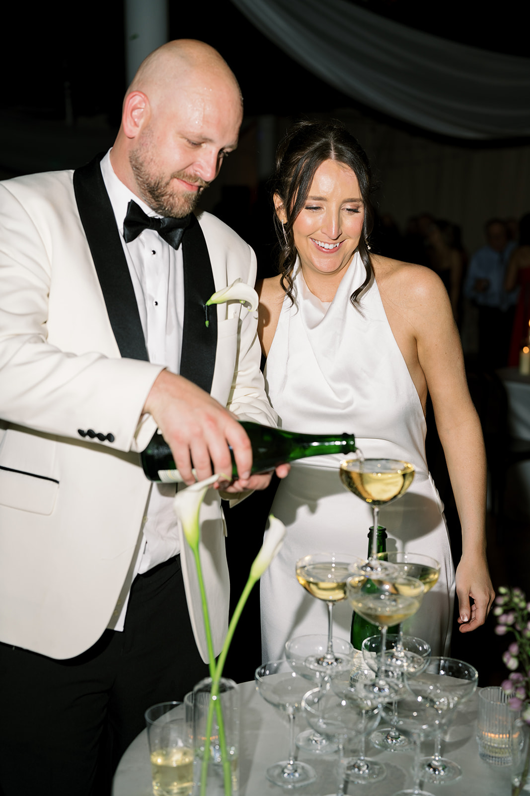Kevin pouring champagne into the coupe-glass tower with Meghan beside him
