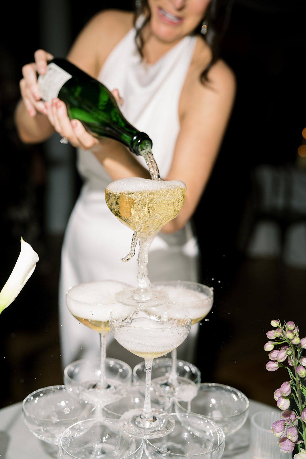 Meghan pouring champagne into a tower of coupe glasses during the reception