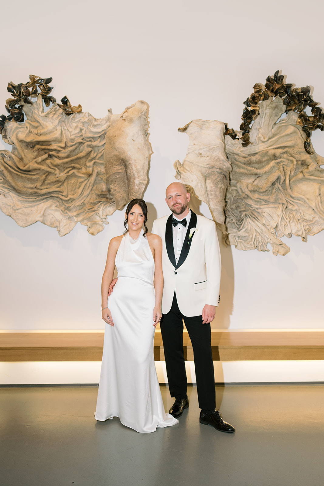 Meghan and Kevin standing together in an art-filled interior during their wedding-day portraits