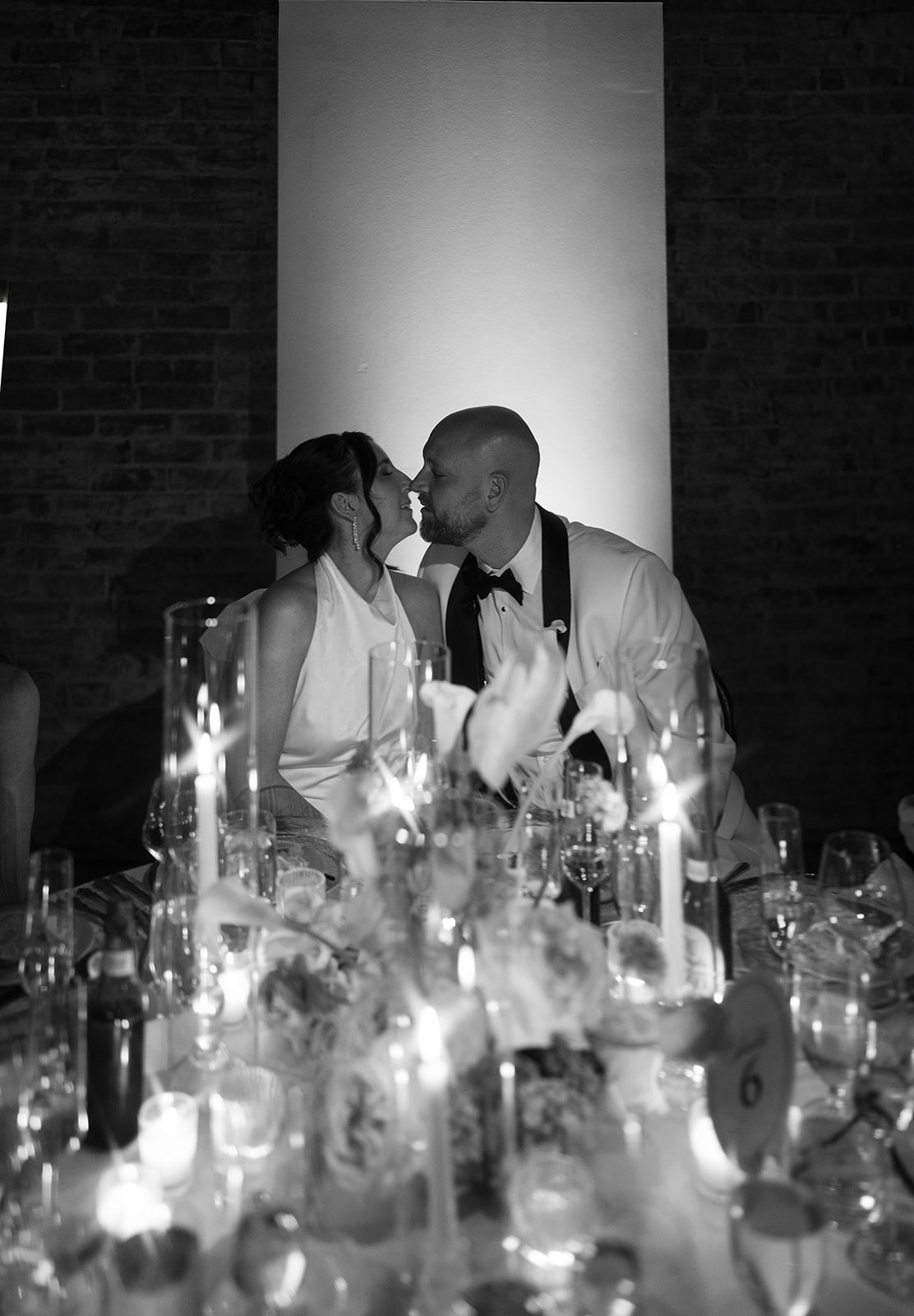 Meghan and Kevin kissing across a candlelit reception table