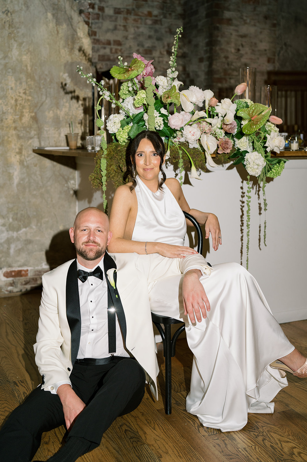 Meghan and Kevin seated together beside a reception floral installation