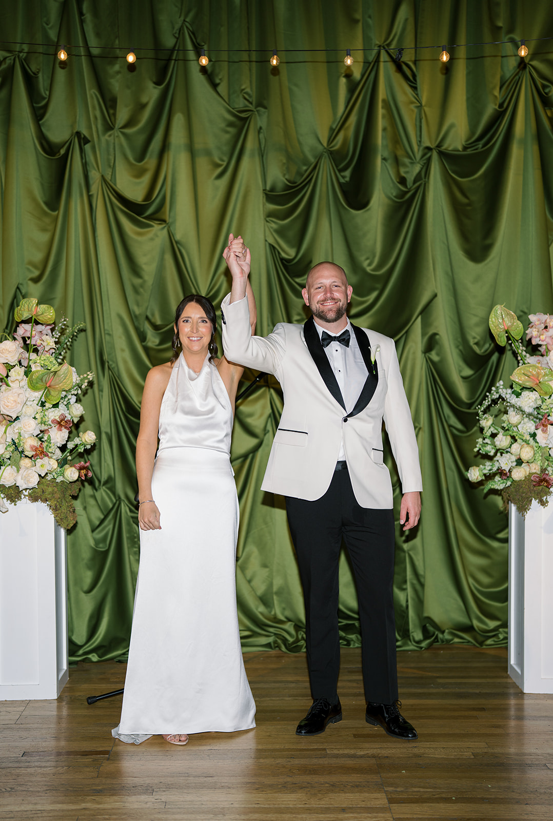 Meghan and Kevin celebrating together in front of deep green drapery