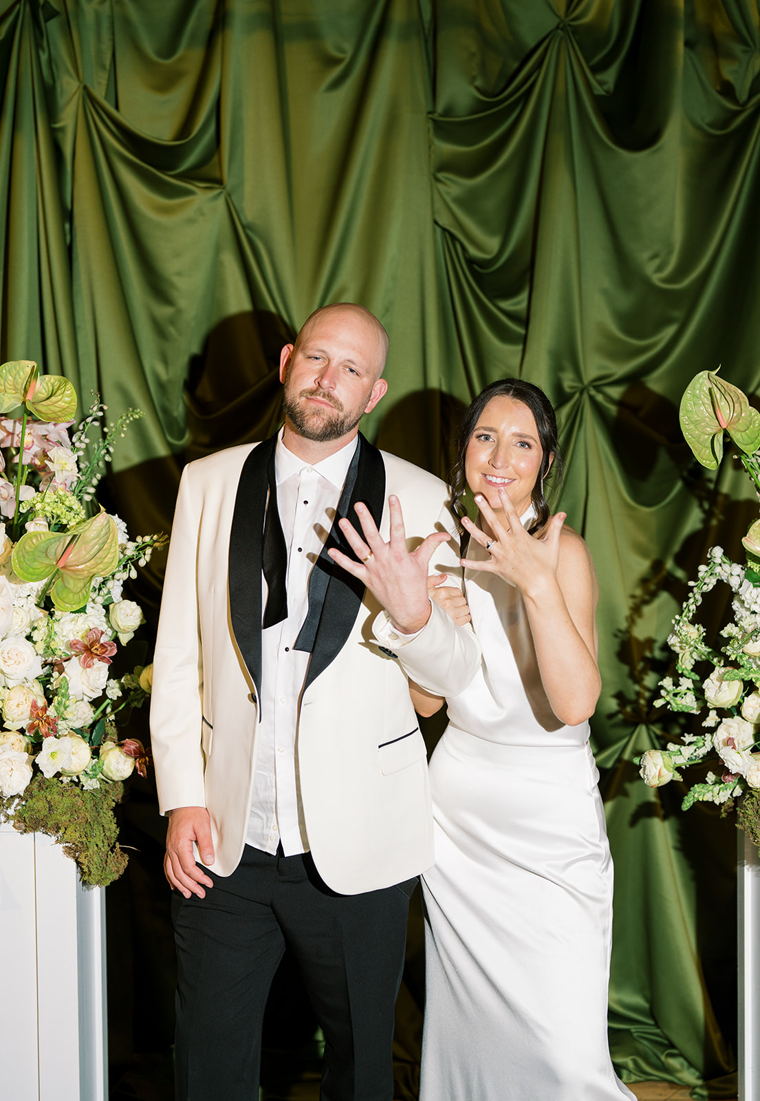 Meghan and Kevin posing together in front of green drapery during the reception