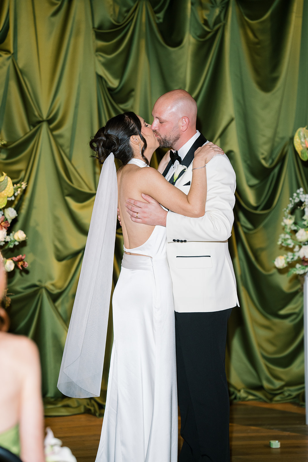 Meghan and Kevin kissing in front of the deep green draped ceremony backdrop