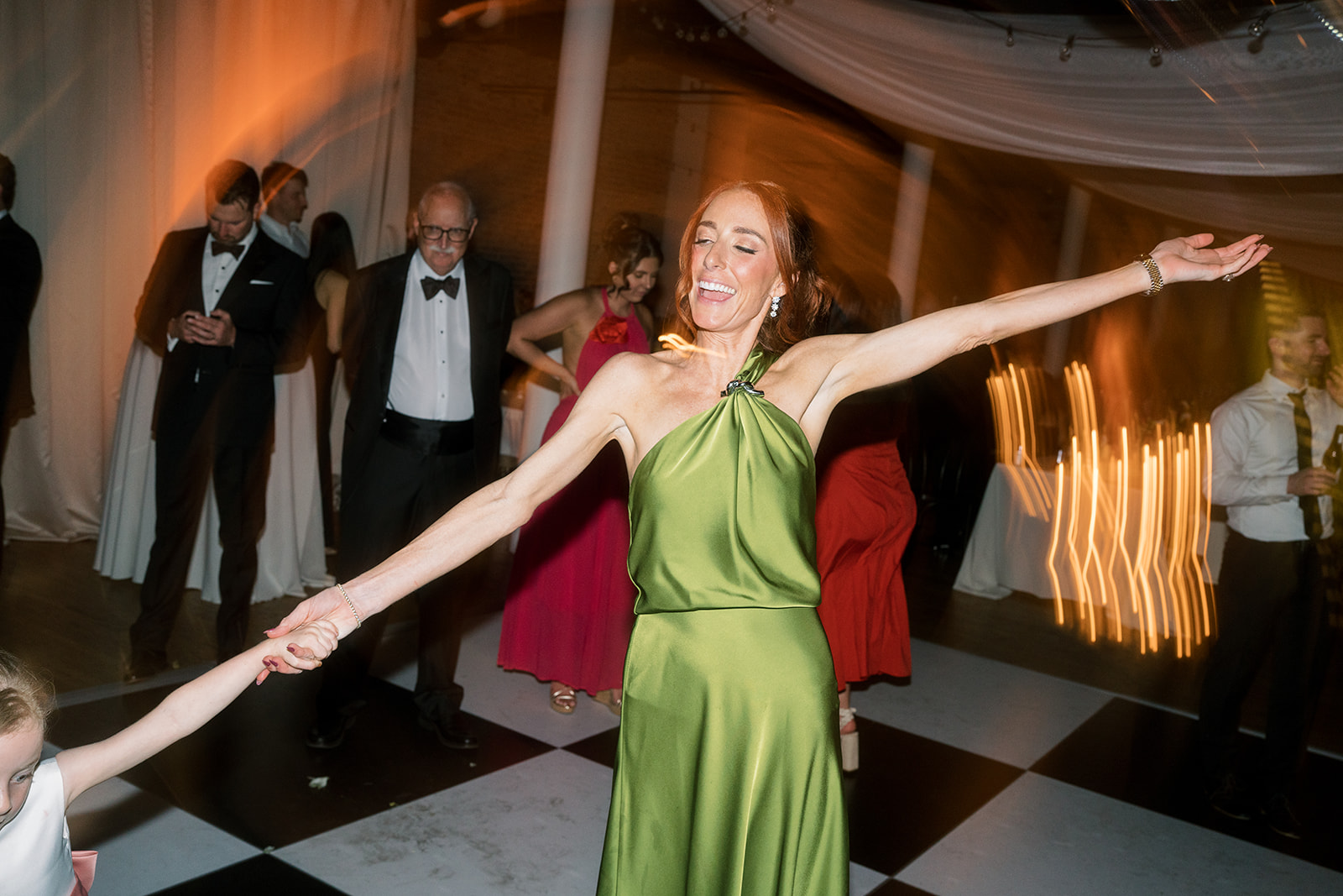 Guest in a green satin dress dancing with arms outstretched at the reception