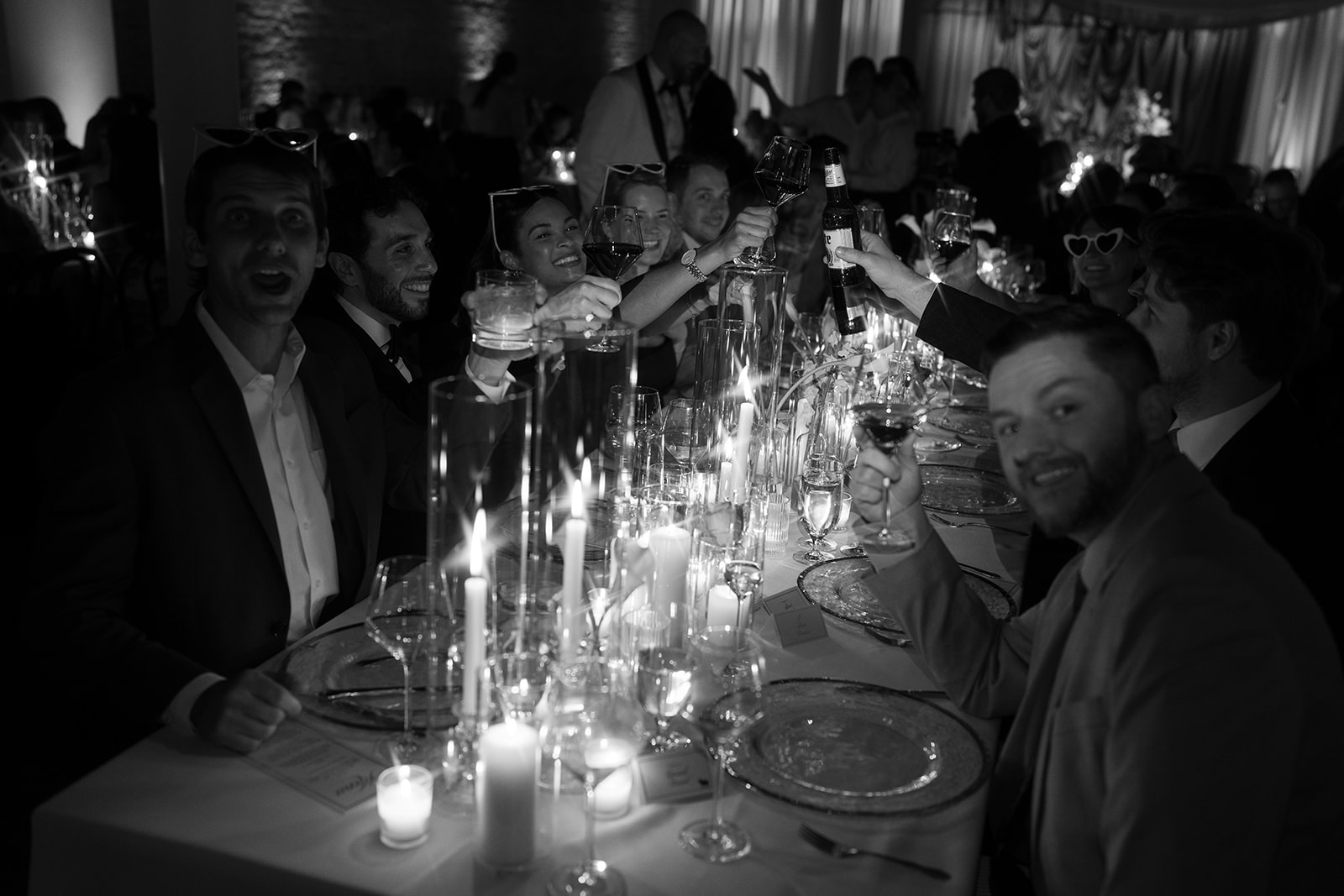 Black-and-white photograph of guests gathered around a candlelit reception table