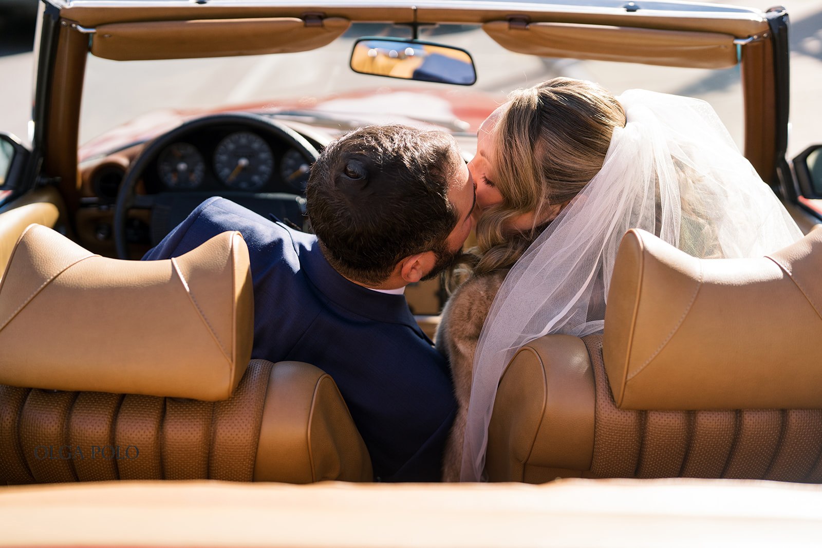 Ryan and Beth kissing in the front seat of a vintage red Mercedes convertible