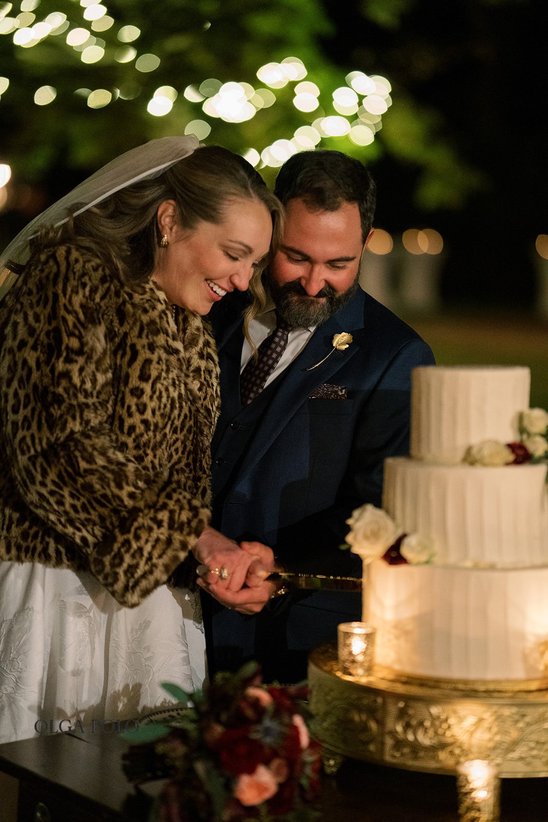 Ryan and Beth cutting their wedding cake beneath string lights