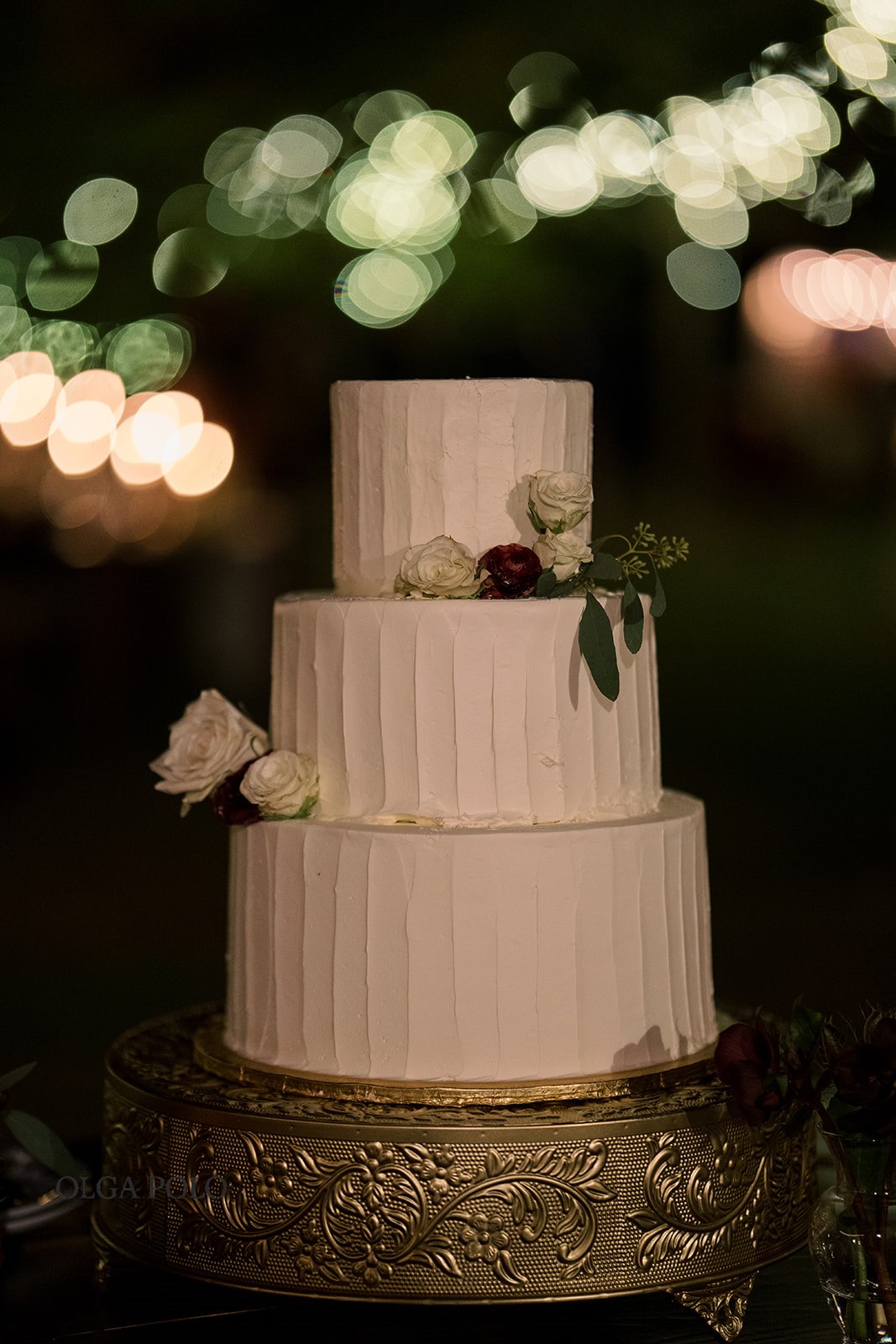 Ryan and Beth standing beside their wedding cake beneath string lights