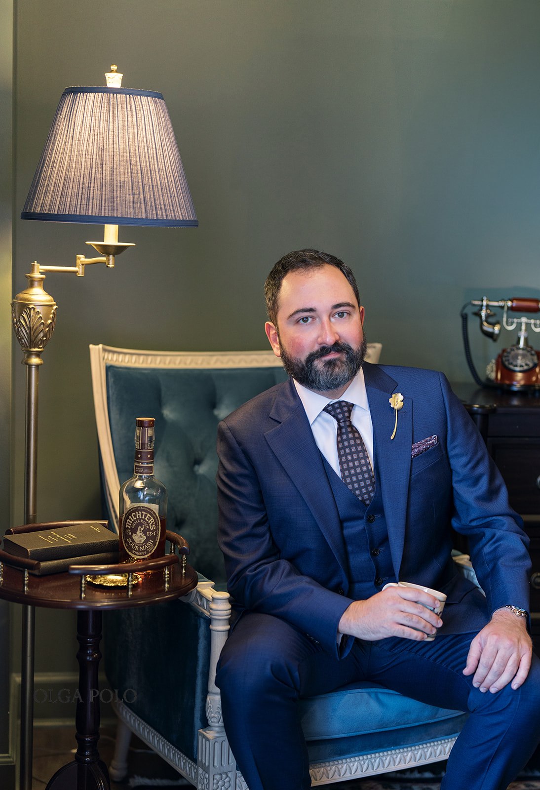 Ryan in a navy suit seated for a groom portrait at The Aldenberg Hotel